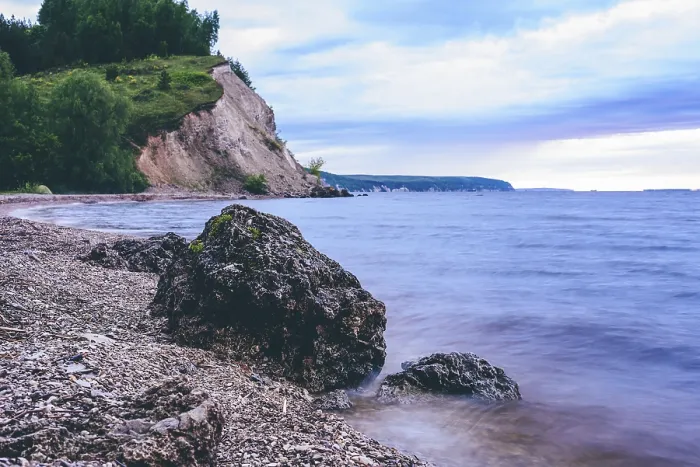 Framed Print : Stone on the riverbank and cliff with birch woodland on background