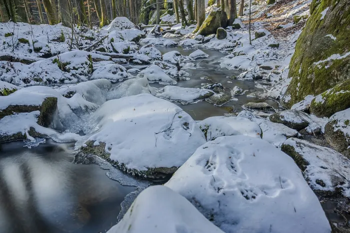 Framed Print : A stream flows calmly through a forest while snow covers the stones and banks
