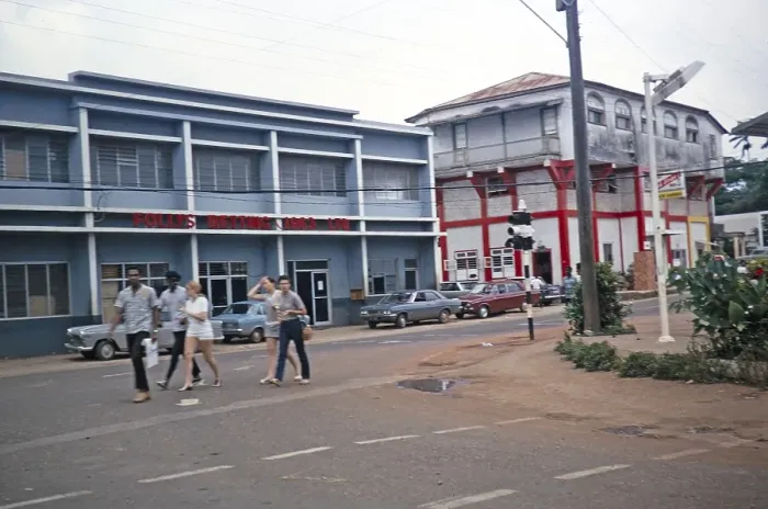 Framed Print : Street scene with people walking past the Follys Betting 1963 Ltd. building, Mandeville, Jamaica, 1970, Central America