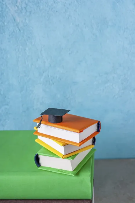 Framed Print : Student paper cap lies on a stack of books on a blue background Framed Print : Student paper cap lies on a stack of books on a blue background