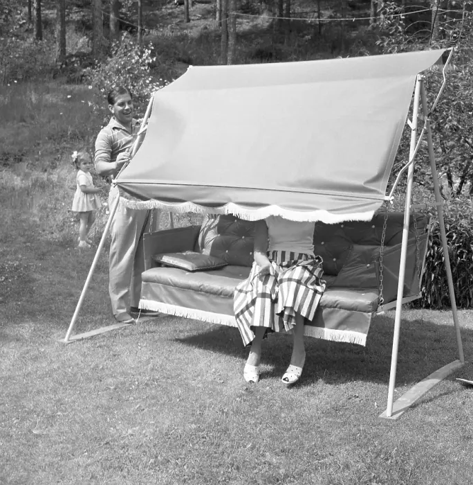 Framed Print : Summer in the 1950s.A woman is sitting in a hammock but her husband plays with her