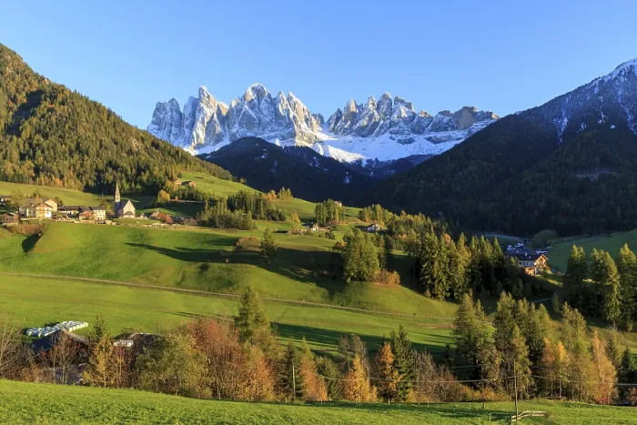 Framed Print : Sunlit village in a valley below a snow-covered mountain range