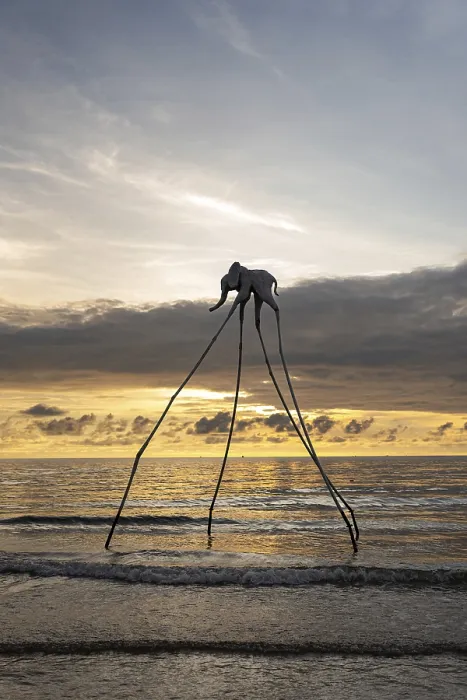 Framed Print : Surreal elephant sculpture with long legs by the ocean at sunset with gentle waves