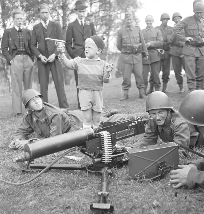 Framed Print : Swedish Soldiers on Regiments day. The new Heavy machine gun is being displayed and showed to the public visiting the grounds. A Young boy has brought his own toy revolver and is joininig in the shooting. Sweden 1942. Kristoffersson ref C17-2
