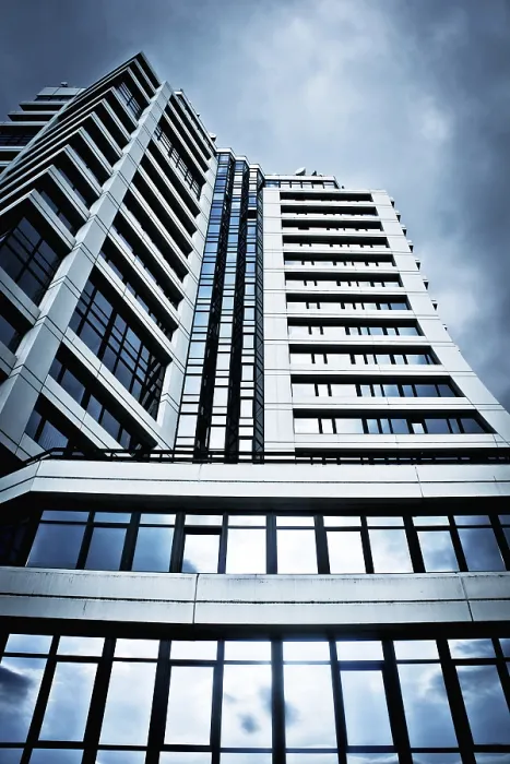 Framed Print : A tall, modern building with glass windows against a cloudy sky Framed Print : A tall, modern building with glass windows against a cloudy sky