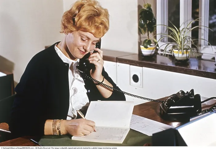 Framed Print : Telephony in the 1960s. An interior of an office room and a woman seen talking on the telephone and taking notes