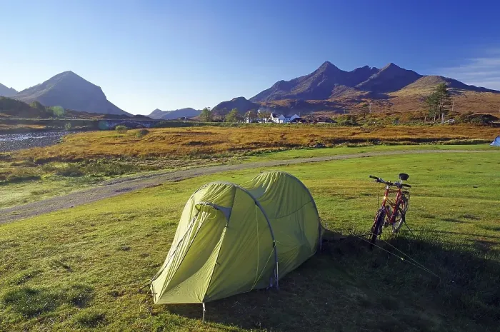 Framed Print : A tent and a bicycle stand on a green meadow with mountains in the background Framed Print : A tent and a bicycle stand on a green meadow with mountains in the background