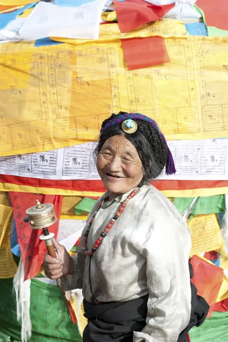 Framed Print : Tibetan Buddhism, devout Tibetan with prayer wheel in front of colorful prayer flags