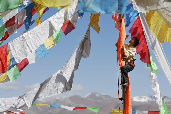 Framed Print : Tibetan pilgrim hanging prayer flags for the upcoming ceremony at Namtso Lake