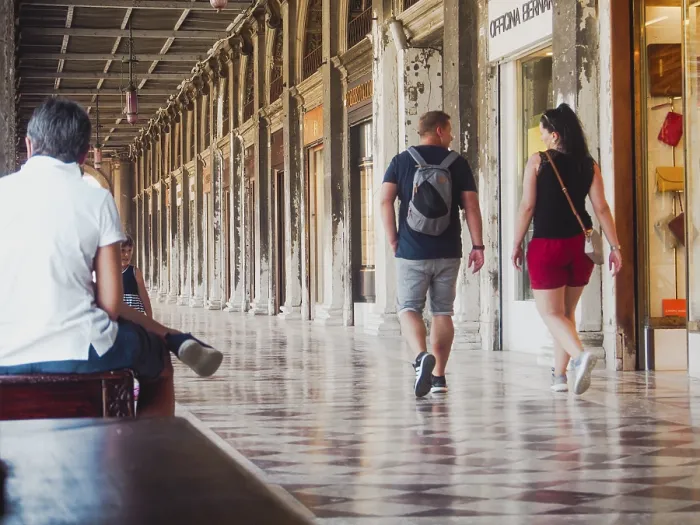 Framed Print : Tourists walk and sit under a covered arcade with historical architecture and mosaic floors