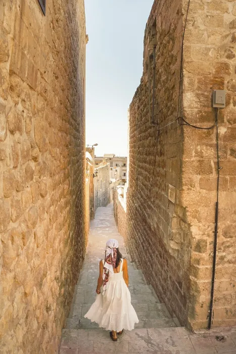 Framed Print : Traveler woman in white dress walking through narrow stone alley in historic city of Mardin Turkey with traditional