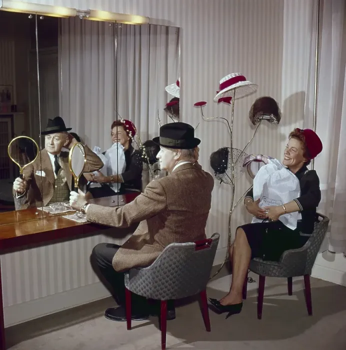 Framed Print : Trying out hats in the 1950s. A couple is sitting in front of a mirror trying hats