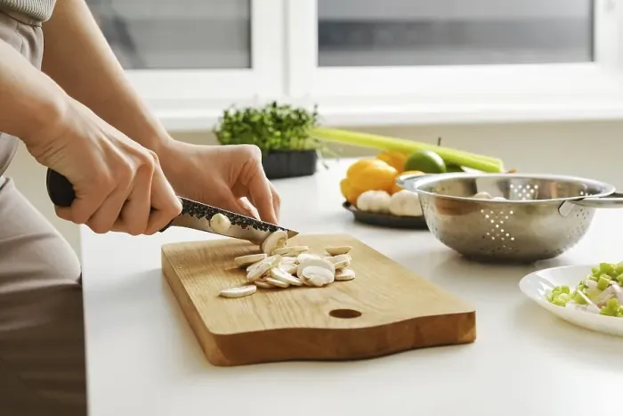 Framed Print : Unrecognizable woman slicing fresh champignon in the kitchen on wooden cutting board