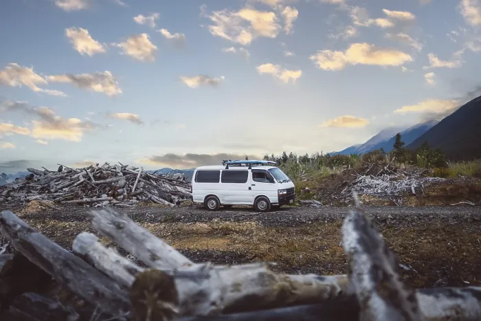 Framed Print : A van stands in a rural area between piles of wood and mountains in the background