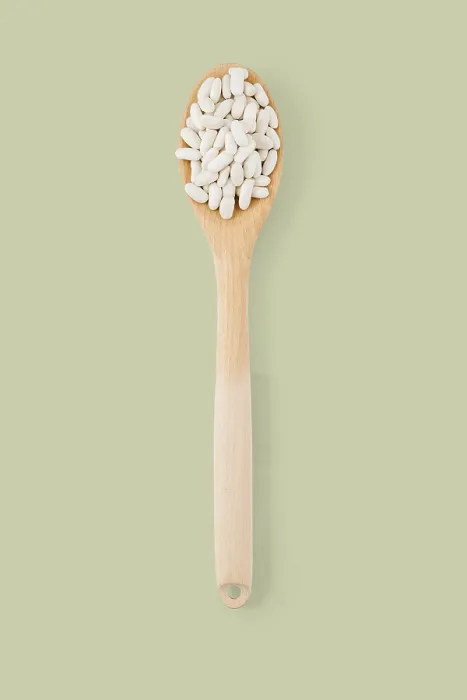 Framed Print : Top view of wooden spoon full of white beans on a green background