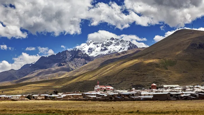 Framed Print : A village at the foot of snow-capped mountains under a blue sky with clouds