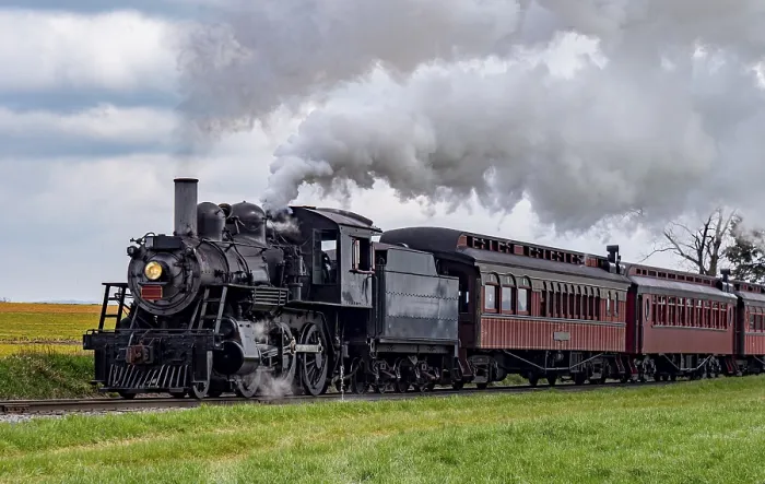 Framed Print : A vintage steam train chugs along railway tracks surrounded by lush green fields under a clear blue sky