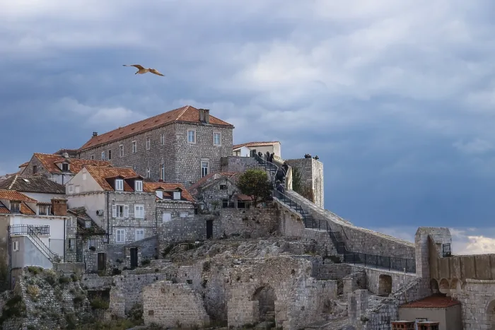 Framed Print : Walkway up to the sunshined stone fortress of Dubrovnik with dramatic cloudscape and gull flying over it Framed Print : Walkway up to the sunshined stone fortress of Dubrovnik with dramatic cloudscape and gull flying over it