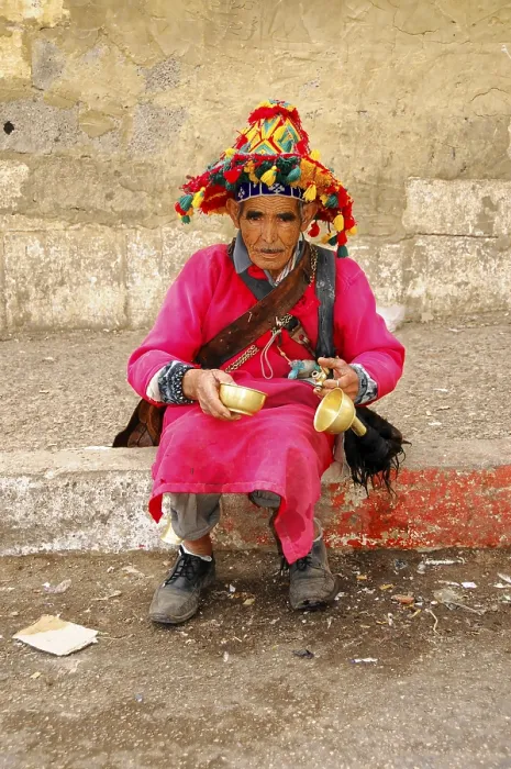 Framed Print : Water vendor, Elderly man in traditional clothes with colourful hat holding bowls and sitting by the road