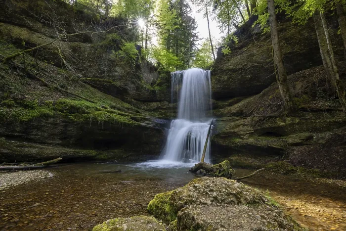 Framed Print : A waterfall in a forest with sunlight shining through the trees and moss-covered rocks