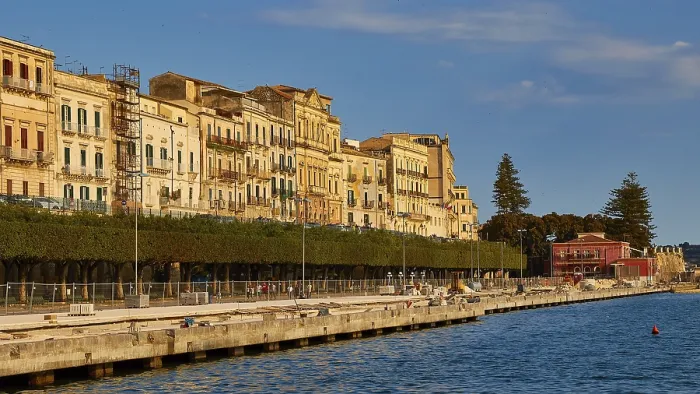 Framed Print : Waterfront with historic buildings and trees under a blue sky