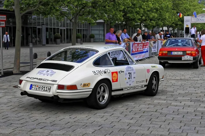 Framed Print : A white Porsche classic car with racing stickers drives through a city street with trees and spectators Framed Print : A white Porsche classic car with racing stickers drives through a city street with trees and spectators