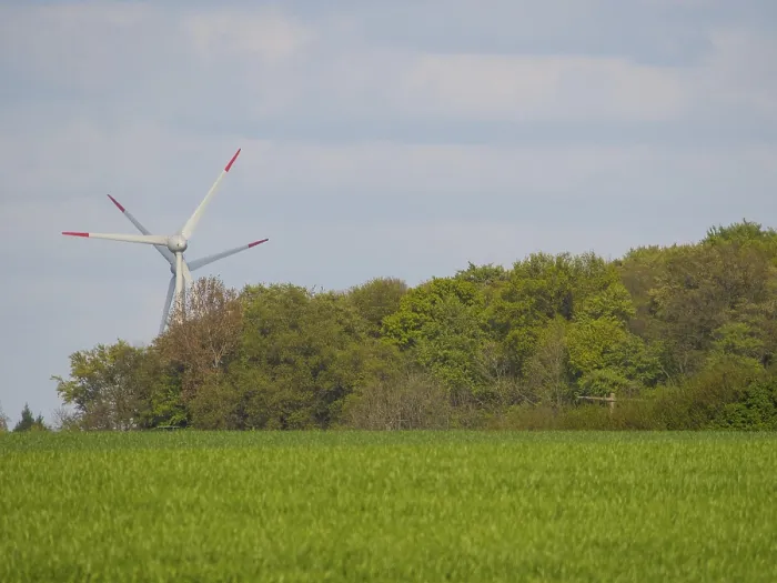 Framed Print : A wind turbine behind green trees and meadows under a cloudy sky