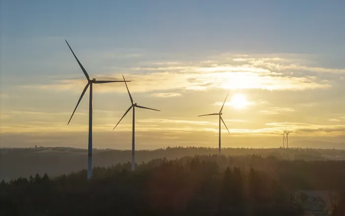 Framed Print : Three wind turbines under a clear sunrise sky over a forest landscape