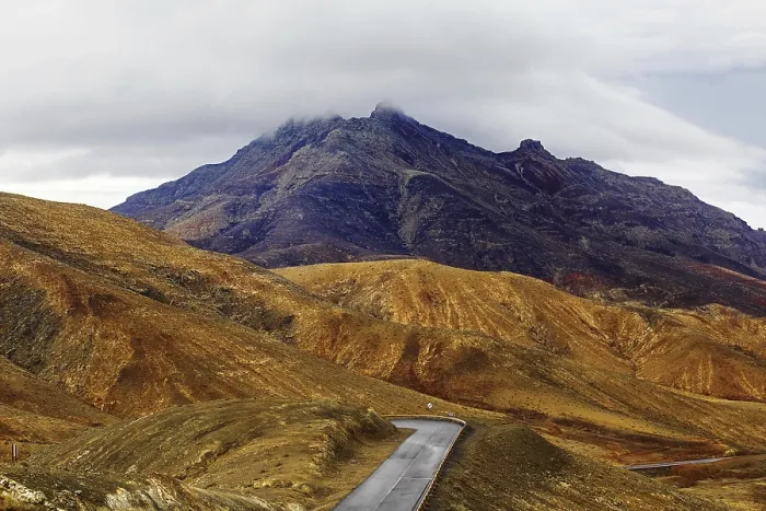 Framed Print : A winding road leads through a mountainous landscape under a cloudy sky
