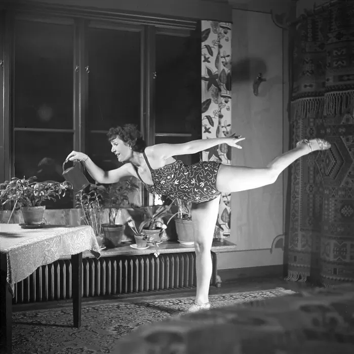 Framed Print : Woman of the 1940s. A woman is seen practising gymnastics while watering the plants in her apartment