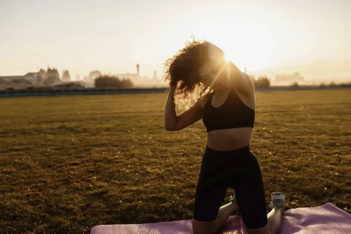 Framed Print : Woman adjusting hair while kneeling on a yoga mat in the sunlight