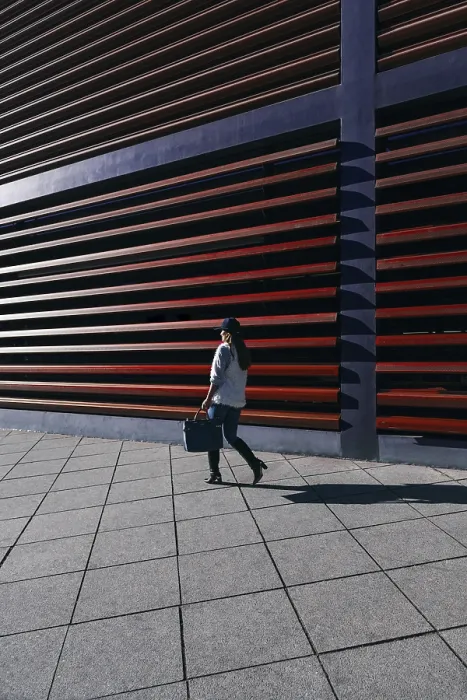 Framed Print : A woman in casual attire walks by a modern building with distinctive horizontal slats Framed Print : A woman in casual attire walks by a modern building with distinctive horizontal slats