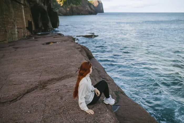 Framed Print : A woman enjoys a serene moment sitting on a rocky ledge overlooking the waves at Flatrock
