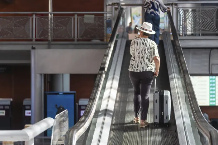 Framed Print : Woman in a hat pulling luggage up an escalator