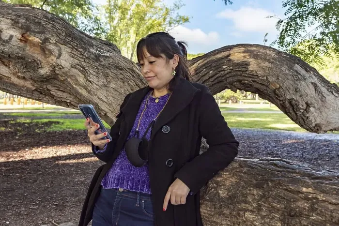 Framed Print : A woman is reading a text message on her mobile phone while leaning on a tree in the park