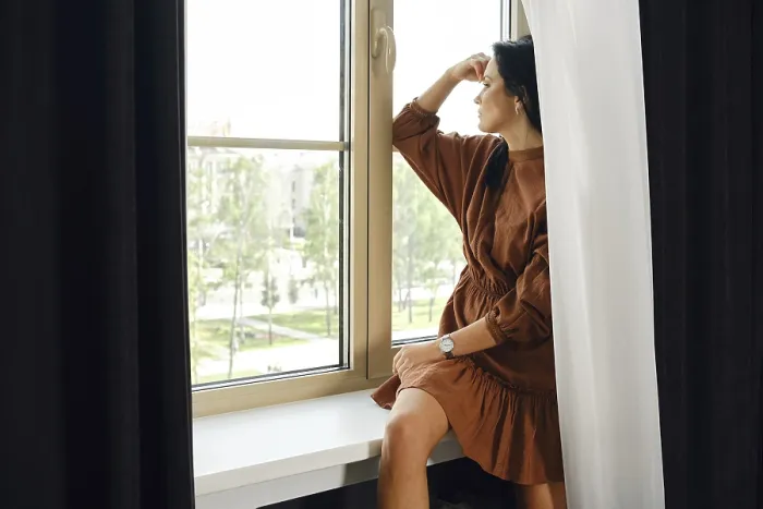 Framed Print : A woman is seated by a window, dressed in a brown dress