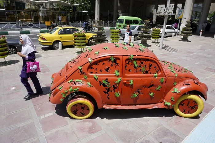 Framed Print : A woman walks past a Volkswagen Beetle art object on the pavement in Tehran