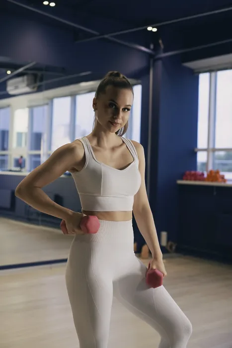 Framed Print : A woman in a white sports outfit is lifting pink dumbbells in a bright gym