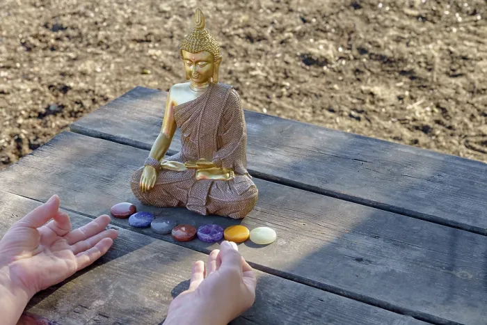 Framed Print : Woman's hands meditating in front of a Buddha statue with colorful chakra stones on a wooden table in a park Framed Print : Woman's hands meditating in front of a Buddha statue with colorful chakra stones on a wooden table in a park