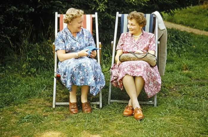 Framed Print : Two women friends sitting in deckchairs on grass lawn one knitting, smiling at each other, England, UK early 1960s