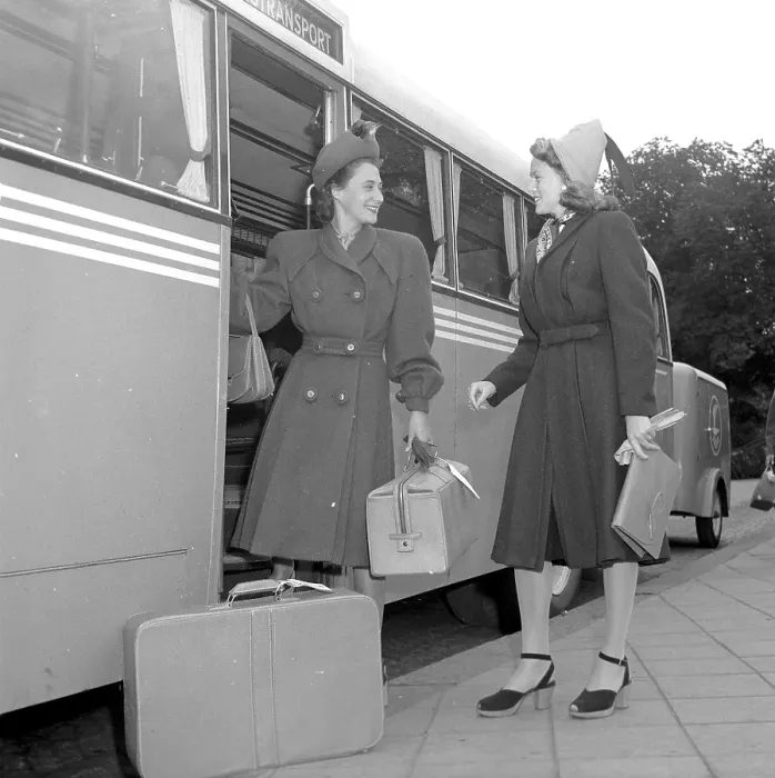 Framed Print : Women's fashion in the 1940s. A young woman in a typical 1940s coat, with matching hat, shoes, gloves and handbag. She steps off the bus carrying her luggage and is greeted by a lady friend also in a typical 1940s coat Framed Print : Women's fashion in the 1940s. A young woman in a typical 1940s coat, with matching hat, shoes, gloves and handbag. She steps off the bus carrying her luggage and is greeted by a lady friend also in a typical 1940s coat