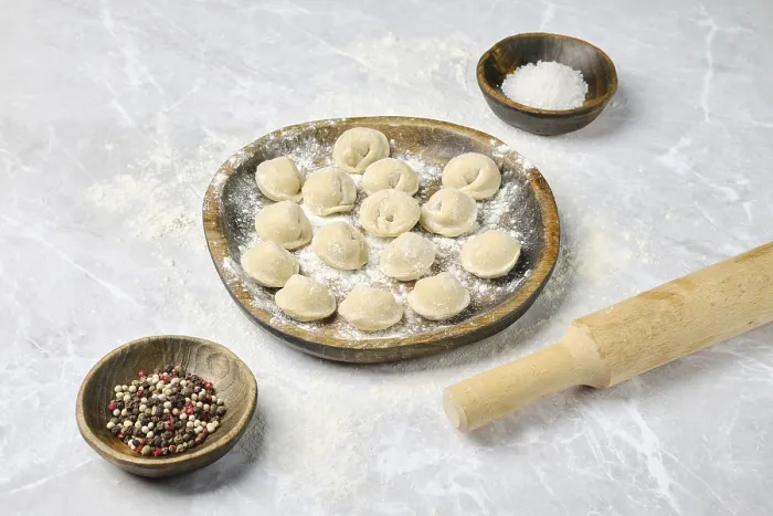 Framed Print : A wooden plate holds freshly made dumplings surrounded by bowls of spices and salt on a flour-dusted countertop