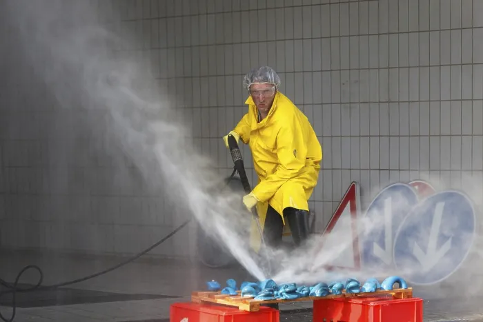 Framed Print : A worker in a yellow protective suit and goggles uses a high-pressure cleaner