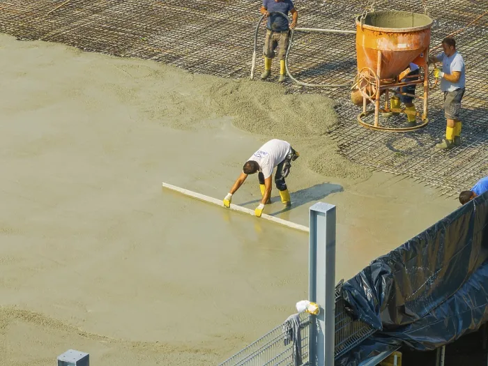 Framed Print : Workers smoothing concrete on a construction site while a concrete mixer stands in the background