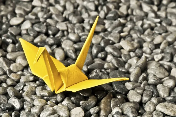 Framed Print : A yellow origami crane sits on a bed of gray pebbles