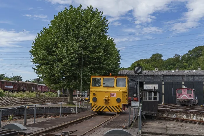 Framed Print : Yellow railway vehicle on rails in front of a tree and depot building