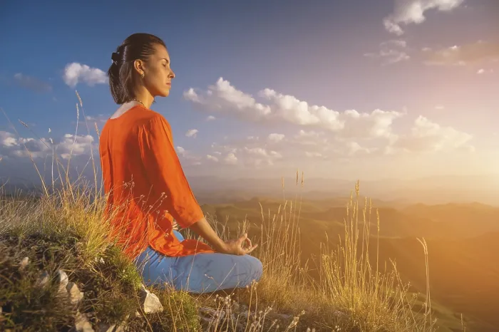 Framed Print : Young caucasian woman meditates in the lotus position in the grass in the mountains near the cliff in the setting sun