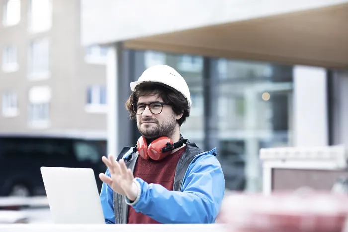 Framed Print : Young engineer with helmet and hearing protection checks outside work with laptop