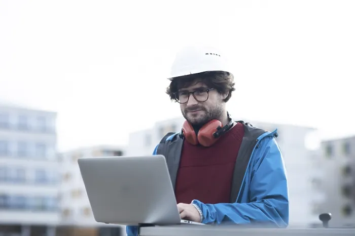 Framed Print : Young engineer with helmet and hearing protection checks outside work with laptop Framed Print : Young engineer with helmet and hearing protection checks outside work with laptop