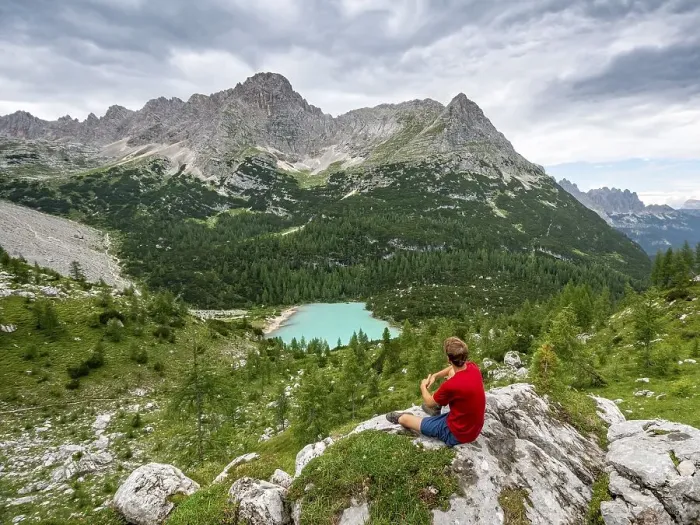 Framed Print : Young man, hiker sitting on rocks and looking at turquoise green Sorapis lake and mountain landscape